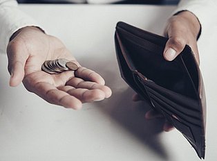 Hand mit Münzen und leerer Geldbörse
